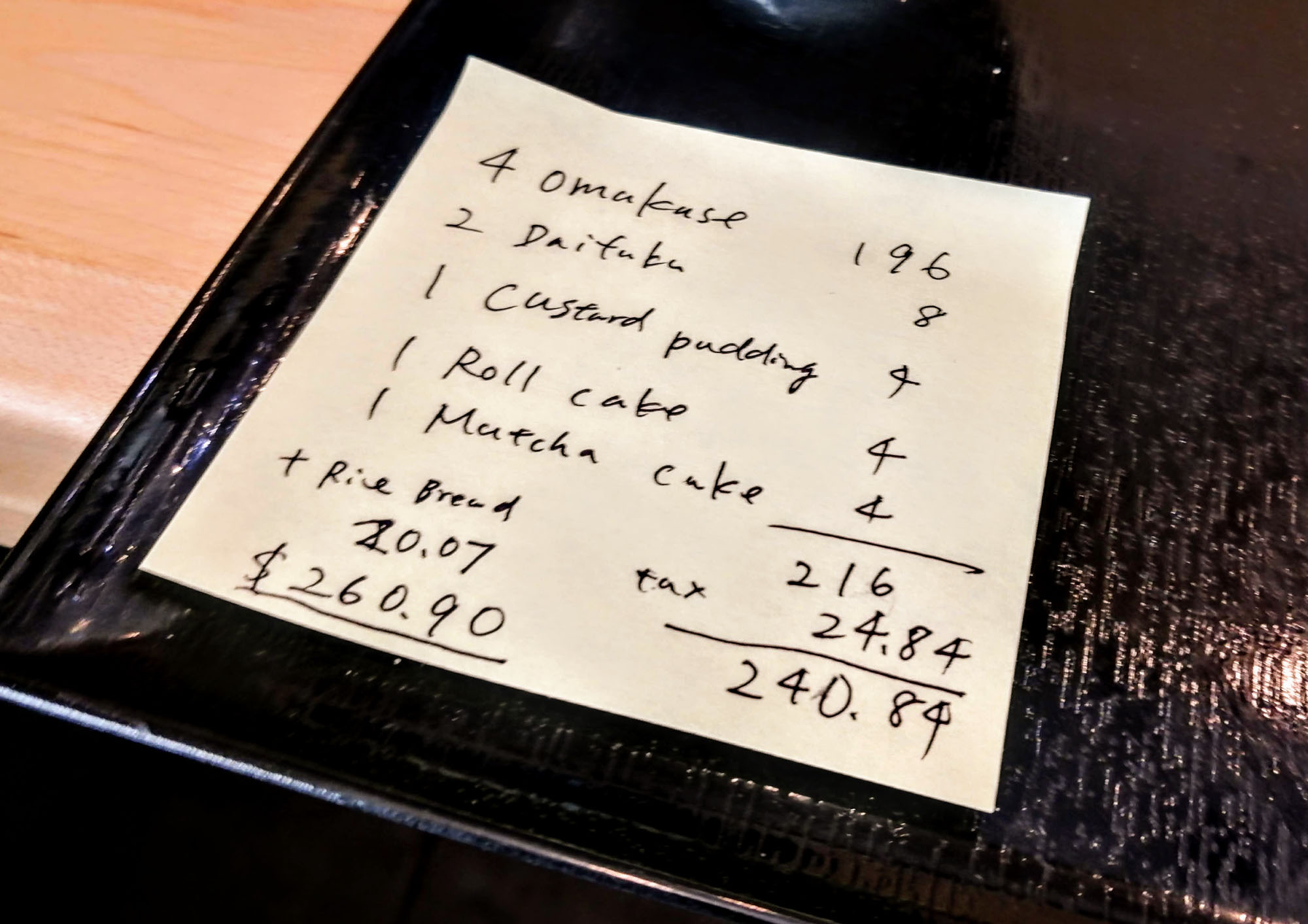 A hand-written post-it note on a black tray listing the cost of each item ordered. Photo by Paul Young.