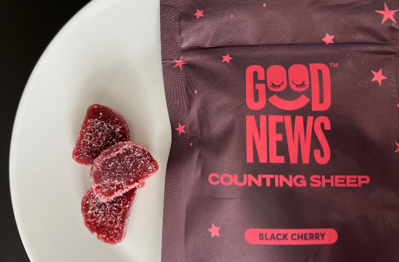 On a white plate, there are three dark red gummies with sugar crystals on the outside beside a brown bag reading Good News Counting Sheep gummies. Photo by Alyssa Buckley.