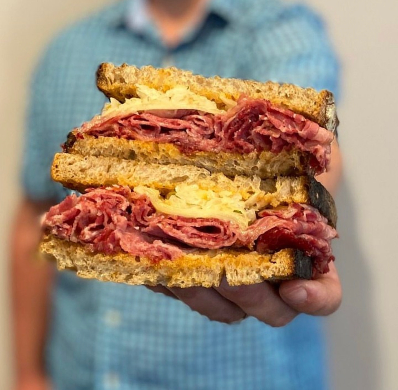 A reuben sandwich is held by a white hand. Photo from Martinelli's Market's Instagram page.