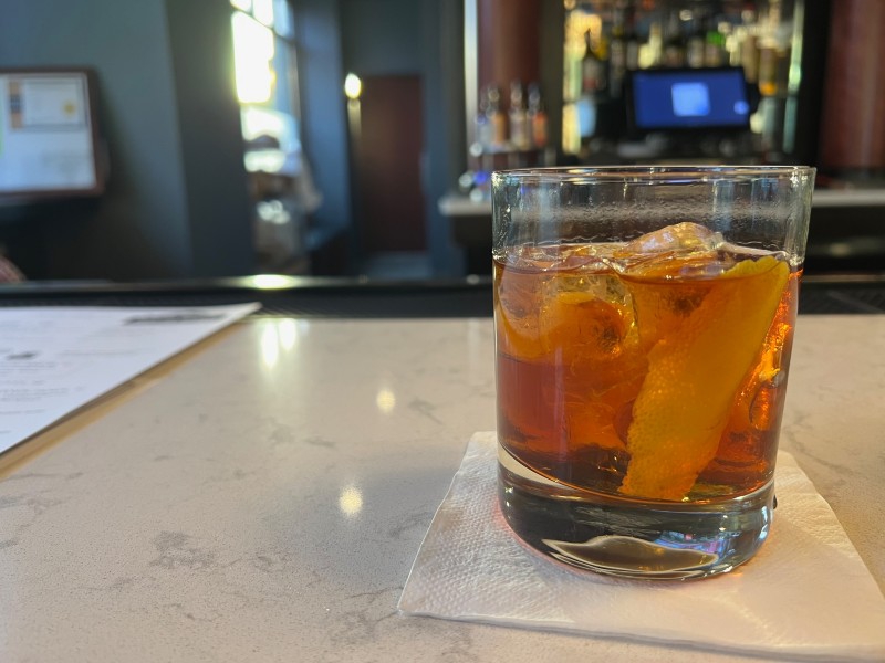 A clear rocks glass filled with brown liquid and an orange peel sits on a bar. Photo by Julie McClure.