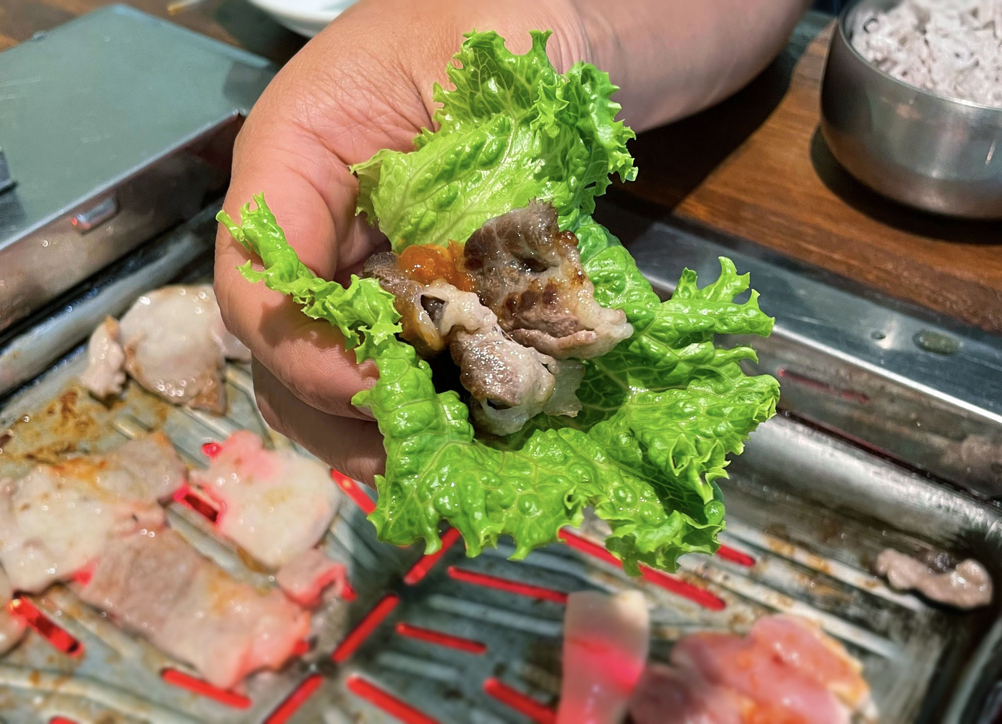 A close-up of a piece of cooked meat wrapped in a lettuce leaf being held by a personâ€™s hand. Photo by Marcus Flinn.