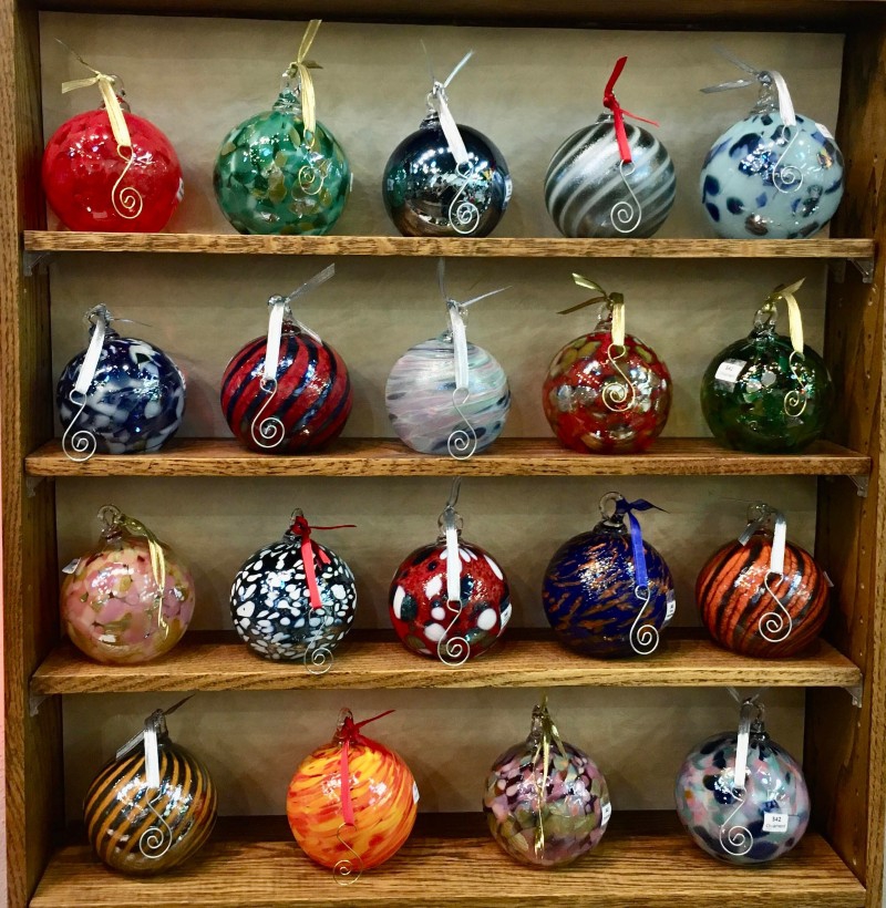 A wooden shelf with rows of colorful handmade glass ornaments. Photo from Prairie Fire Glass Facebook page.