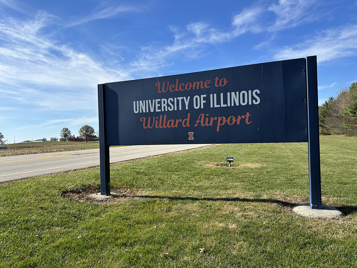 A dark blue rectangular sign that says University of Illinois in white block letters, and Welcome to Willard Airport in orange script.