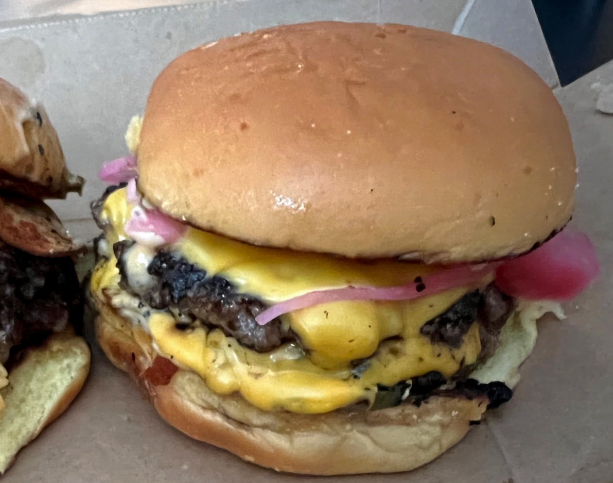 In a takeout box, there is a smashburger by the Weird Meat Boyz with two patties and American cheese dripping down the side. Photo by Alyssa Buckley.