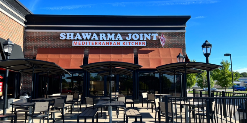 The exterior of Shawarma Joint's second location in Urbana has outdoor seating and orange awnings below the restaurant's name. Photo by Alyssa Buckley.