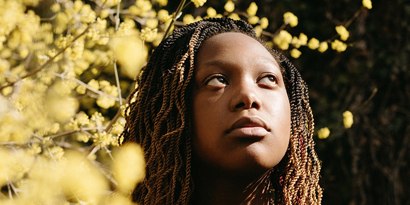  Close-up portrait of Danyla Nash looking up and to her left. Standing outside beside a tree with golden-yellow leaves. Photo by Anna Longworth-Singer.