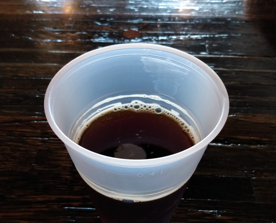 The barrel-aged bock blend. A dark beer in a plastic cup is resting on a dark wood table. Photo by Michael O'Boyle.