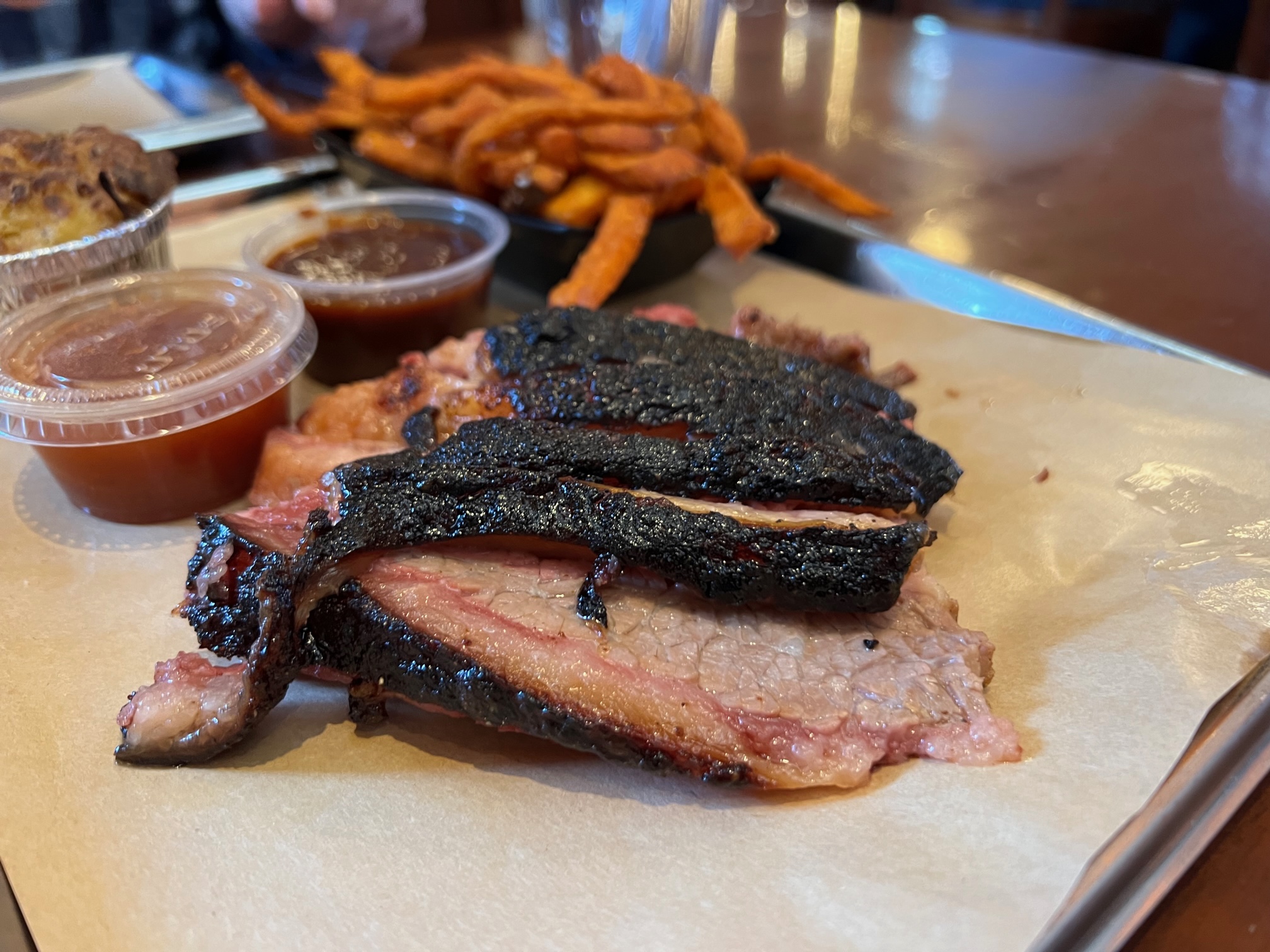 On a metal tray at Black Dog Smoke & Ale, there is a half pound of burnt ends, two side cups of sauce, a side of sweet potato fries, and a side of twice baked potato casserole. Photo by Alyssa Buckley.