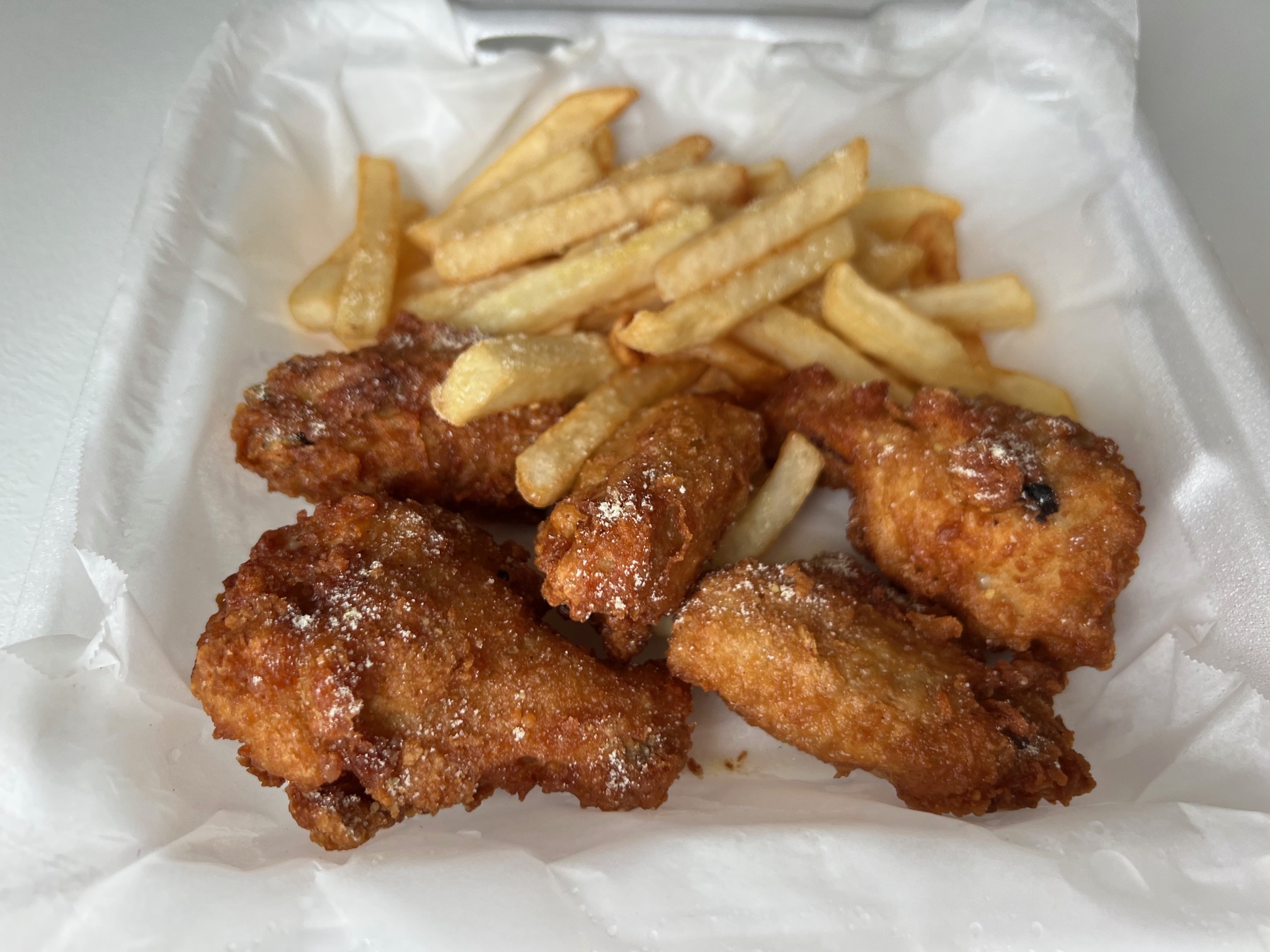 Five wings from Garro's Taste of the City are in a styrofoam box with a side of fries. Photo by Alyssa Buckley.
