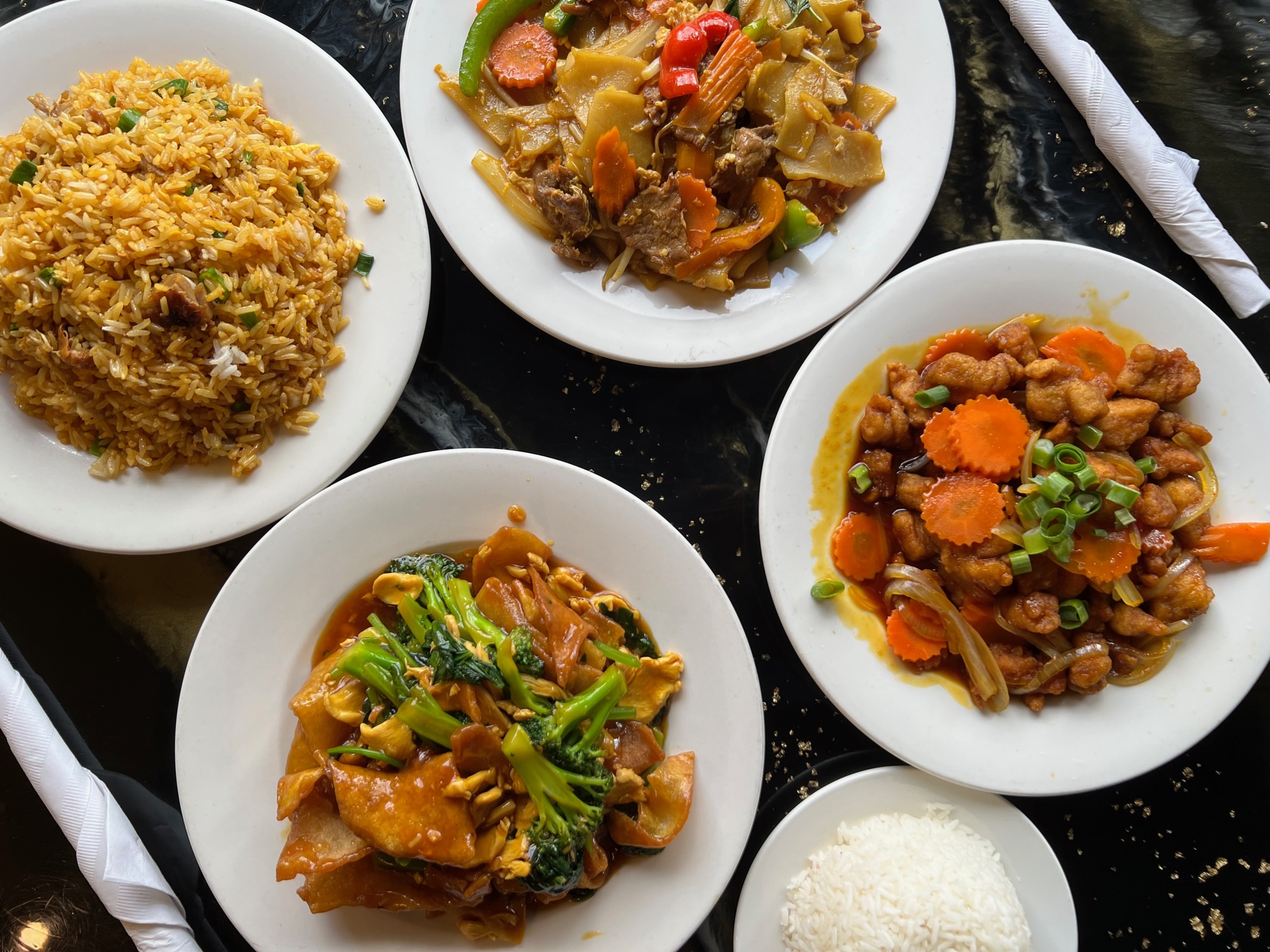 An overhead photo shows four Thai dishes on a shiny black table. Photo by Alyssa Buckley.
