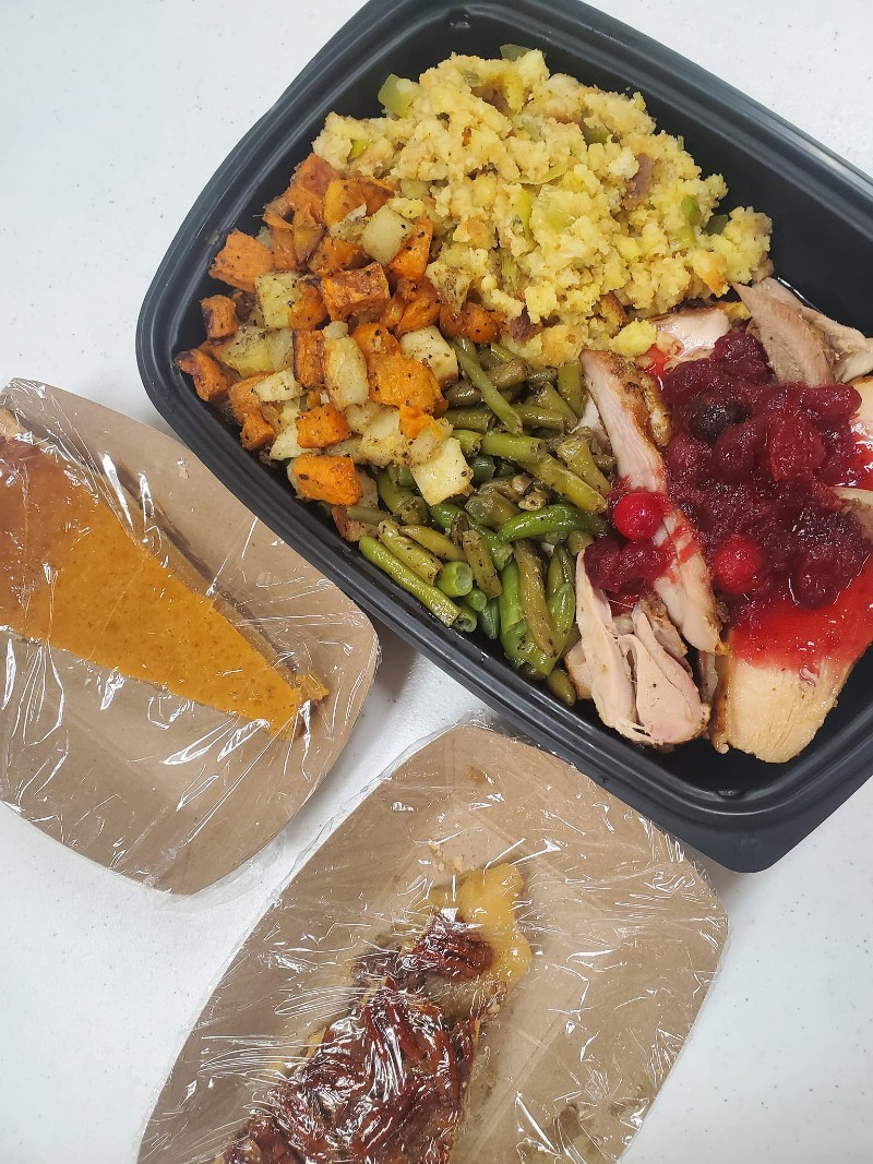 A black plastic container holds a Thanksgiving meal including turkey, green beans, stuffing, potatoes, and cranberry sauce. There are two paper containers with pieces of pie next to it. Photo from Community UCC Facebook page.