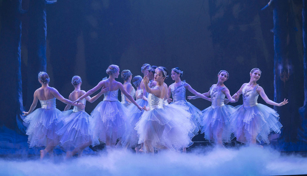 snow scene from the nutcracker shows ballerinas in white tutus dancing on stage amongst white mist