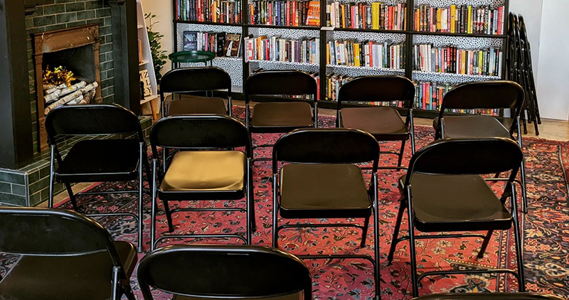 Chairs set up in the Literary's reading corner with a brick fireplace to the right and shelves of books in the background. Photo from the Literary's Facebook page.