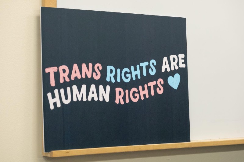A black sign sits on the ledge of a white dry erase board. In bubble letters with the words alternating in light pink, light blue, and white it says â€œTrans Rights are Human Rights.â€ Photo from LGBT Resource Center Facebook page.