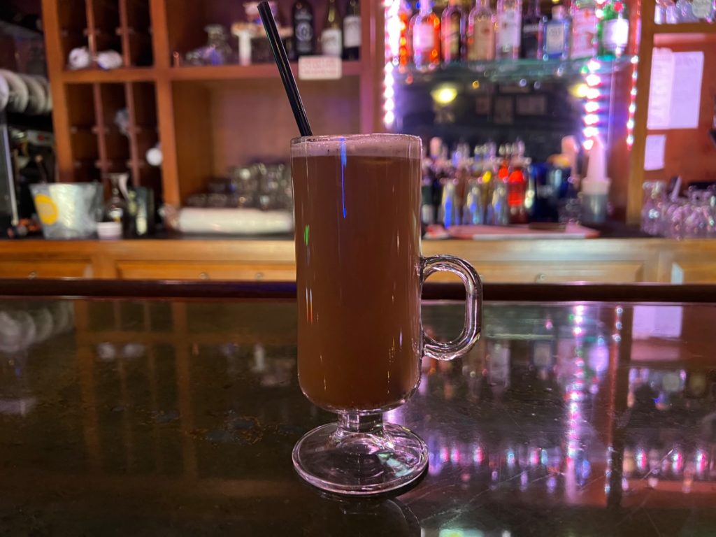 A hot buttered rum at Bentley's Pub in Champaign, Illinois is on the bar with a black straw. Photo by Alyssa Buckley.