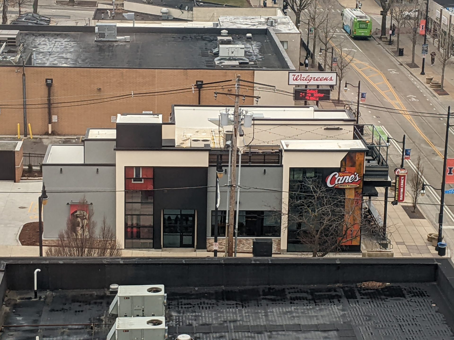 View from above of a building with a gray, black, and cream colored exterior. There is a Raising Cane's sign on one side. Across the roof are string lights.