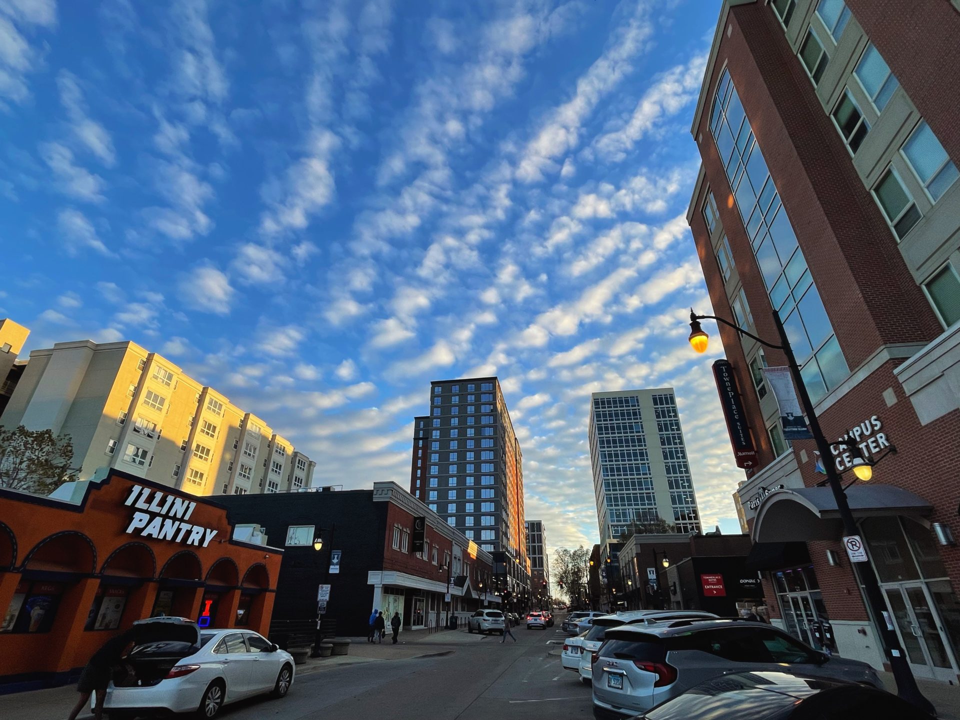 A fish eye view of Campustown, with tall buildings along the horizon and a blue sky streaked with thin white clouds.
