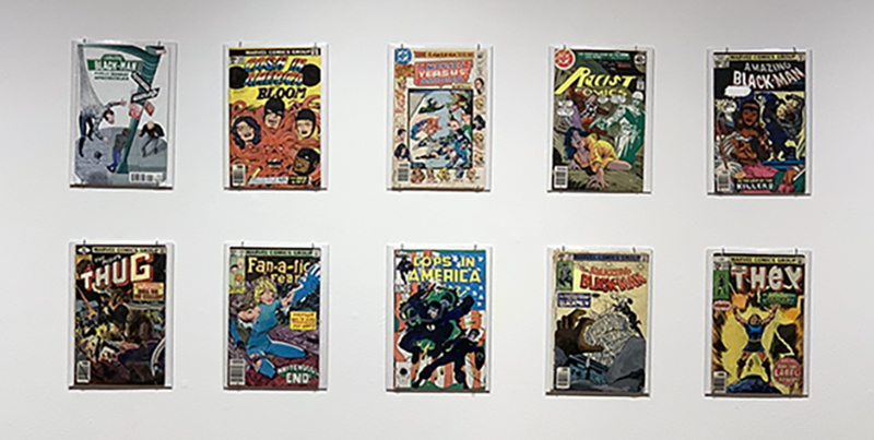 Ten of Kumasi J. Barnett's handpainted comic book covers in plastic sleeves hung on a white wall.