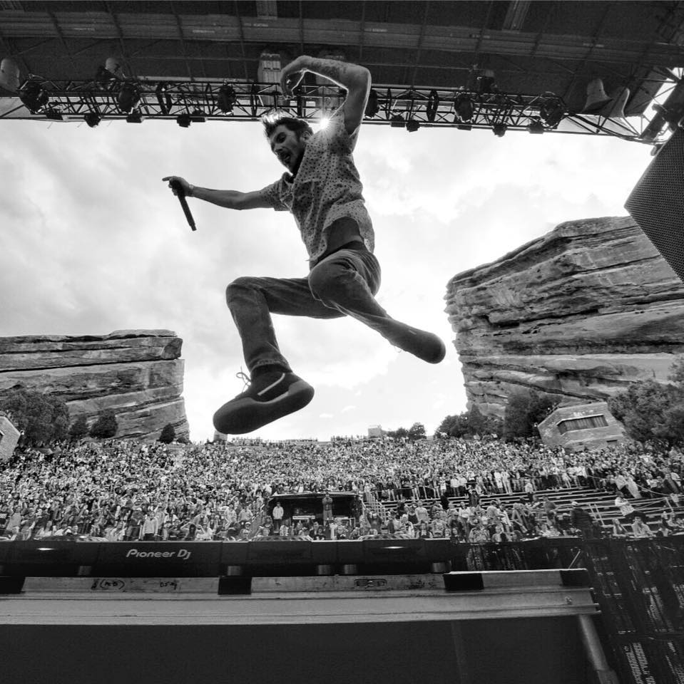 DJ Dirt Monkey performs at Red Rocks Amphitheater. He jumps in the air as the crowd cheers him on.