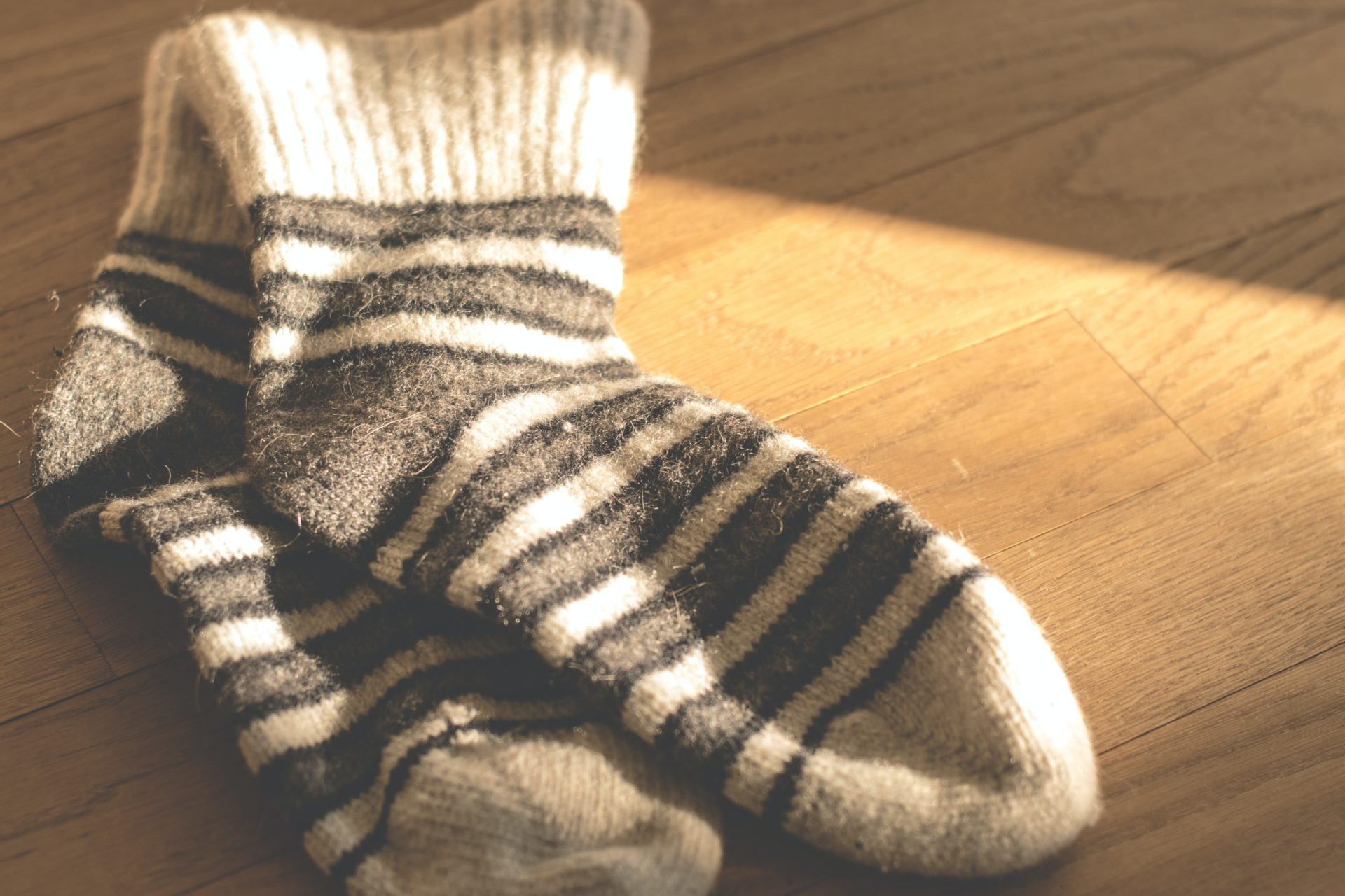 A pair of white and gray striped fuzzy socks are sitting on a light wood floor.