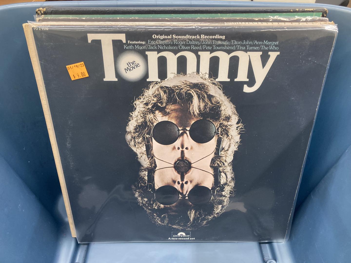 Album cover of Tommy original soundtrack recording. The word Tommy is in large white block letters at the top. There's a photo of a man with wavy hair and circular black sunglasses in the center of the album cover. 