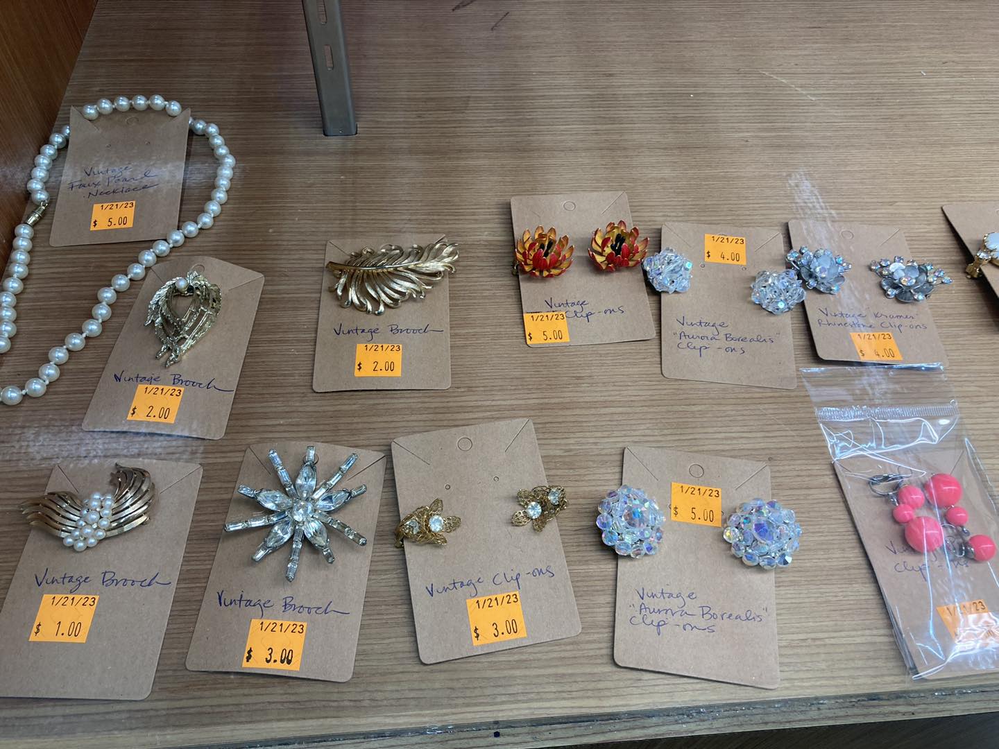 A collection of vintage looking brooches and earrings attached to brown cardboard with orange price stickers.