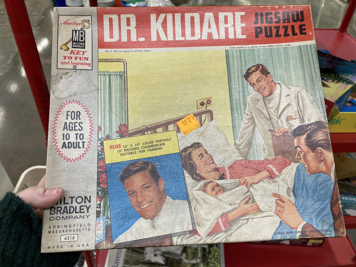 An old Dr. Kildare jigsaw puzzle box. The picture on the front is of a women in a hospital bed holding a baby, with a doctor in a lab coat looking over and a man at the end of the bed talking.