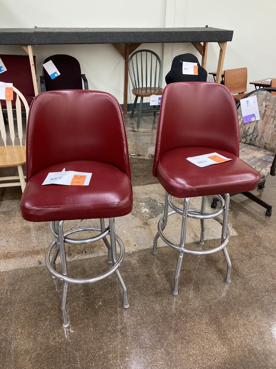 Two hi-top chairs. They are dark red vinyl with stainless steel bases. 