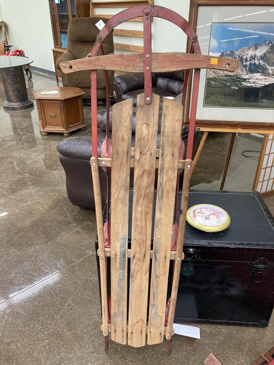 An old school wooden toboggan with red metal runners is propped up on a black trunk.