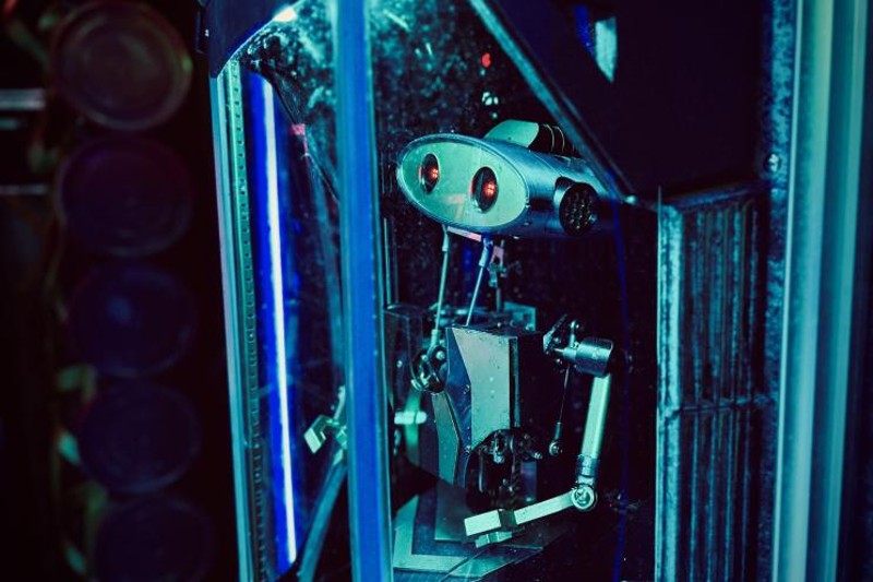 A robot with red lights for eyes seems to be in a glass case. 