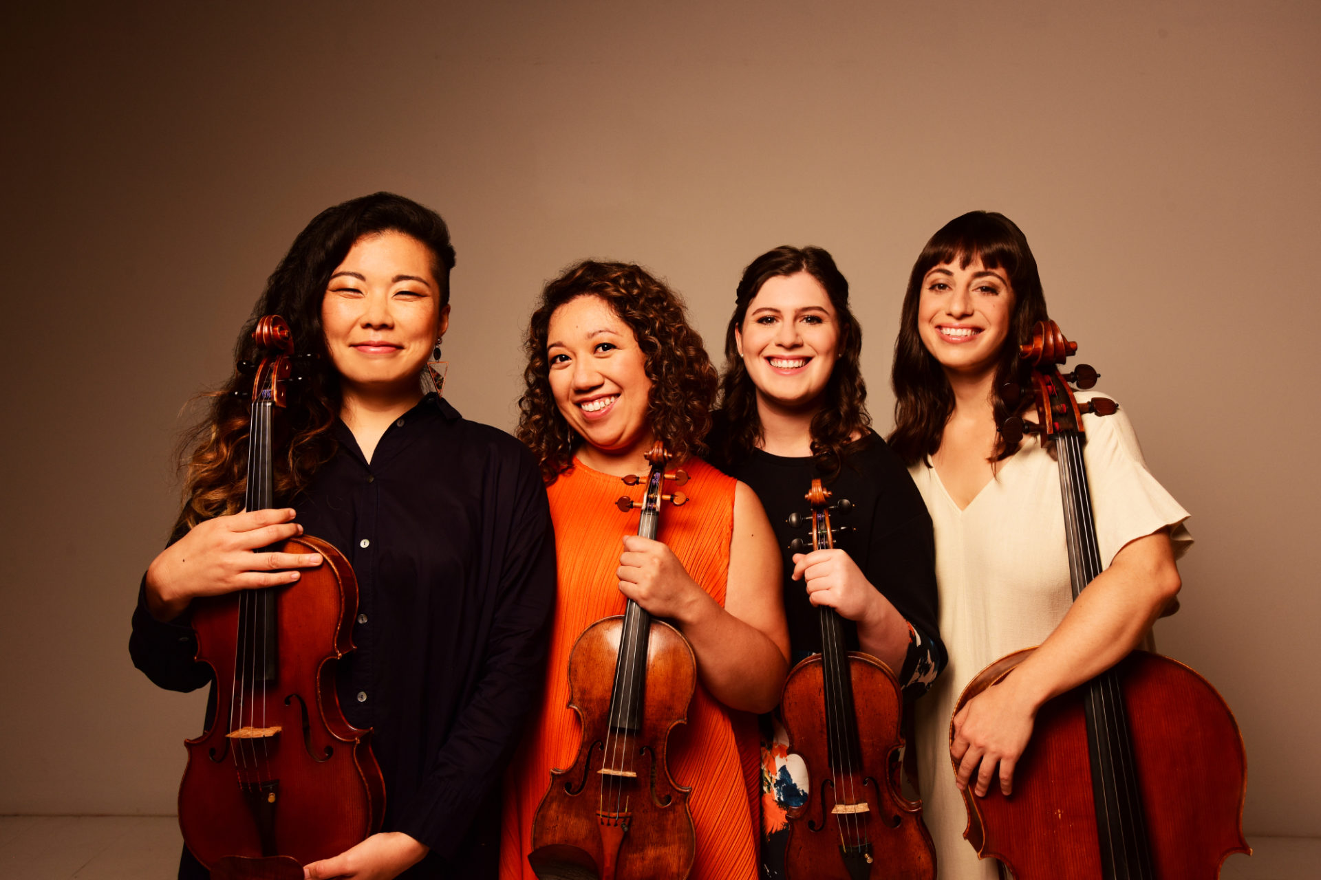 Four women are pictured with their string instruments. The background is a neutral brown and beige.