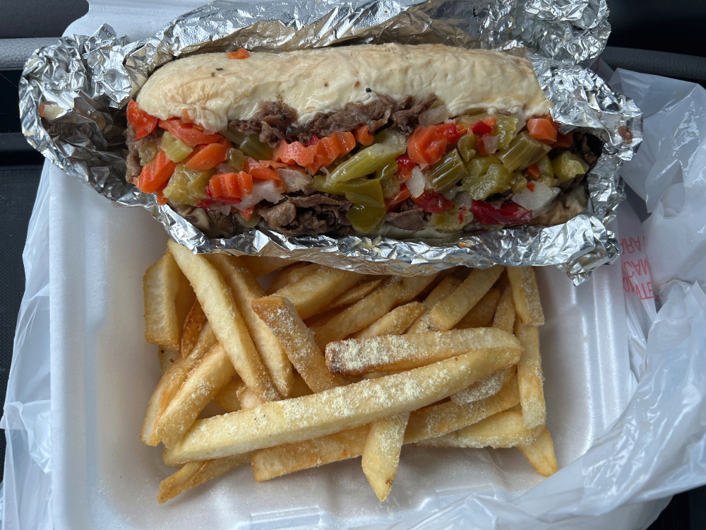 An overhead photo of an Italian beef sandwich unwrapped but atop tin foil on top of seasoned fries. This is part of the author's list of February foods to try from Black-owned restaurants in Chanmpaign-Urbana. Photo by Alyssa Buckley.