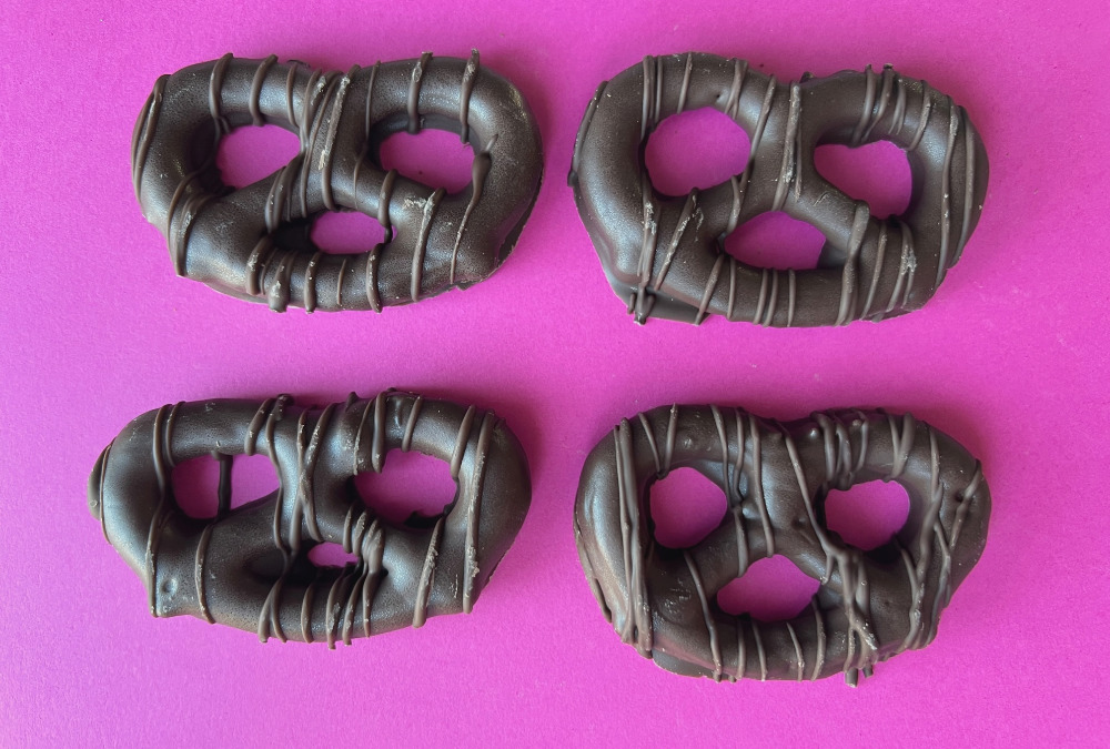 Four chocolate covered pretzels from Cool Bliss Popped Bliss in Champaign, Illinois are arranged in a 2x2 grid atop a hot pink piece of paper. Photo by Alyssa Buckley.
