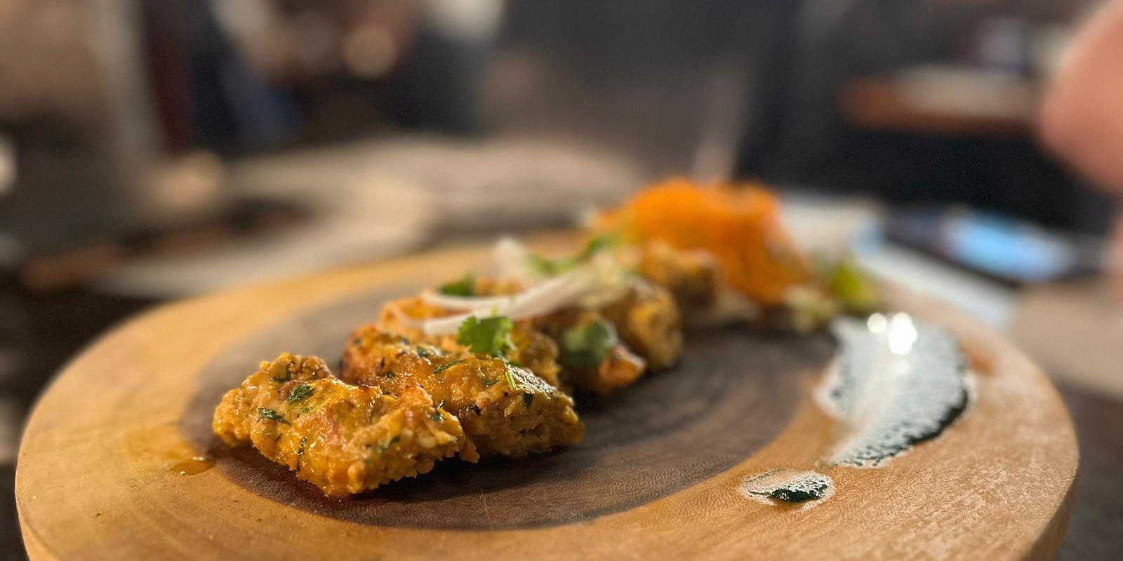 Himalayan Chimney's reshmi chicken kababs beautifully plated on a wooden stump platter with a smear of a white sauce. Photo byRashmi Tenneti.