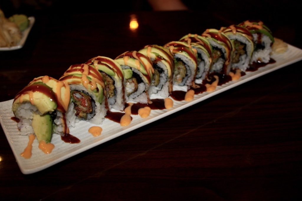 Spider bomb roll at Sushi Siam. Ten pieces of sushi served on a long, white, rectangular plate. The each piece is garnished with a dark brown and an orange sauce. Photo by Rebecca Wells