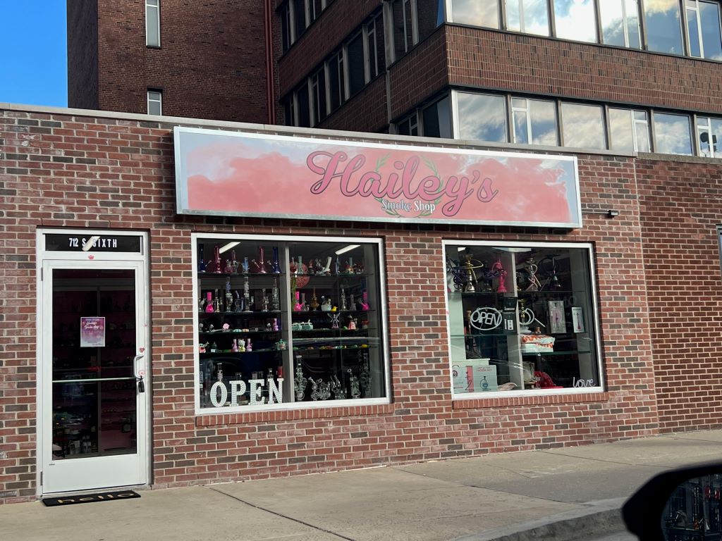 The brick facade of a one story building. It has a large rectangular sign that says Hailey's in pink script. Two large windows sit below the sign.