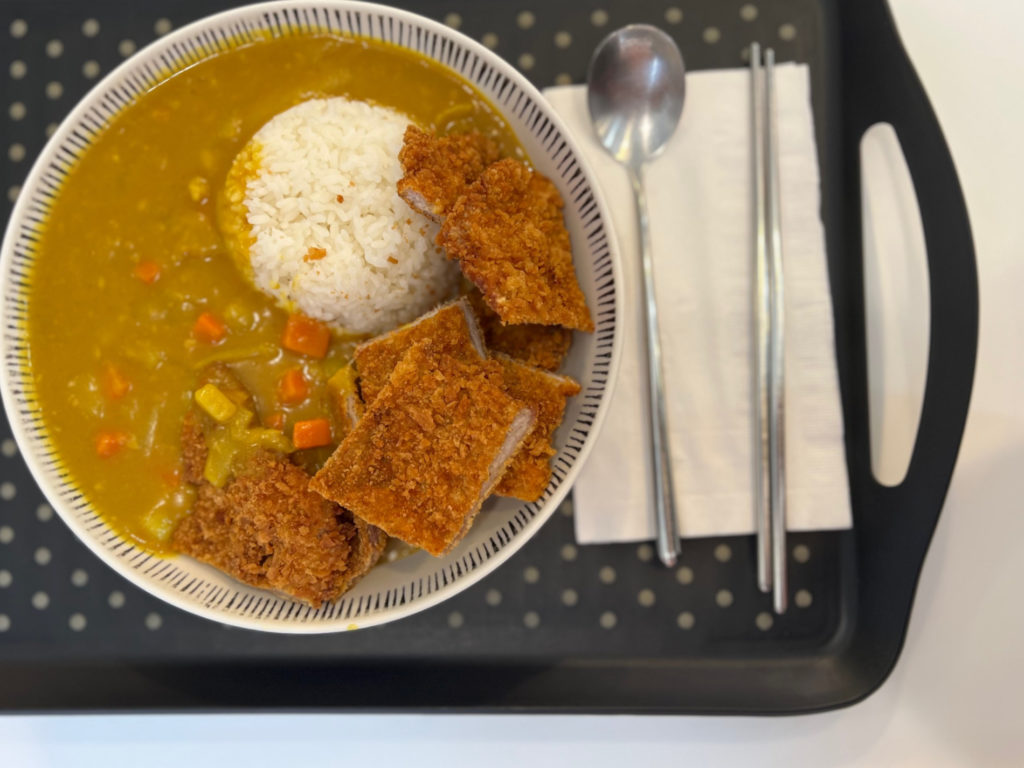 Curry pork tonkatsu has crispy pork cutlets beside a mound of rice flooded with yellow curry with potatoes and carrots. Photo by Alyssa Buckley.