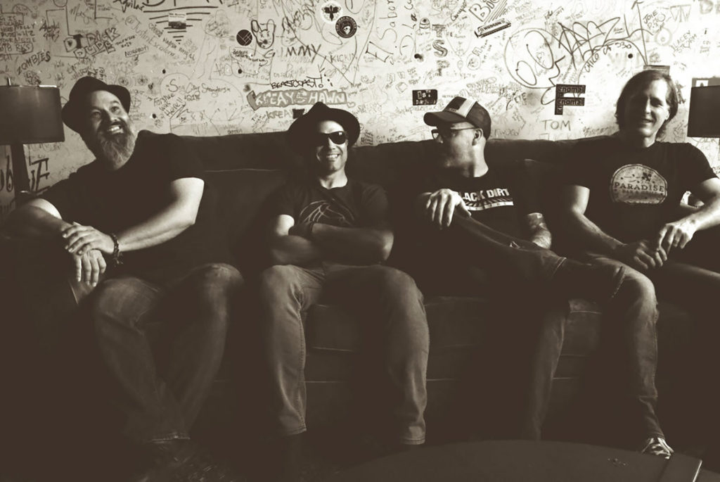 The four members of Backyard Tire Fire sitting on a couch in front of a wall with much graffiti on it.