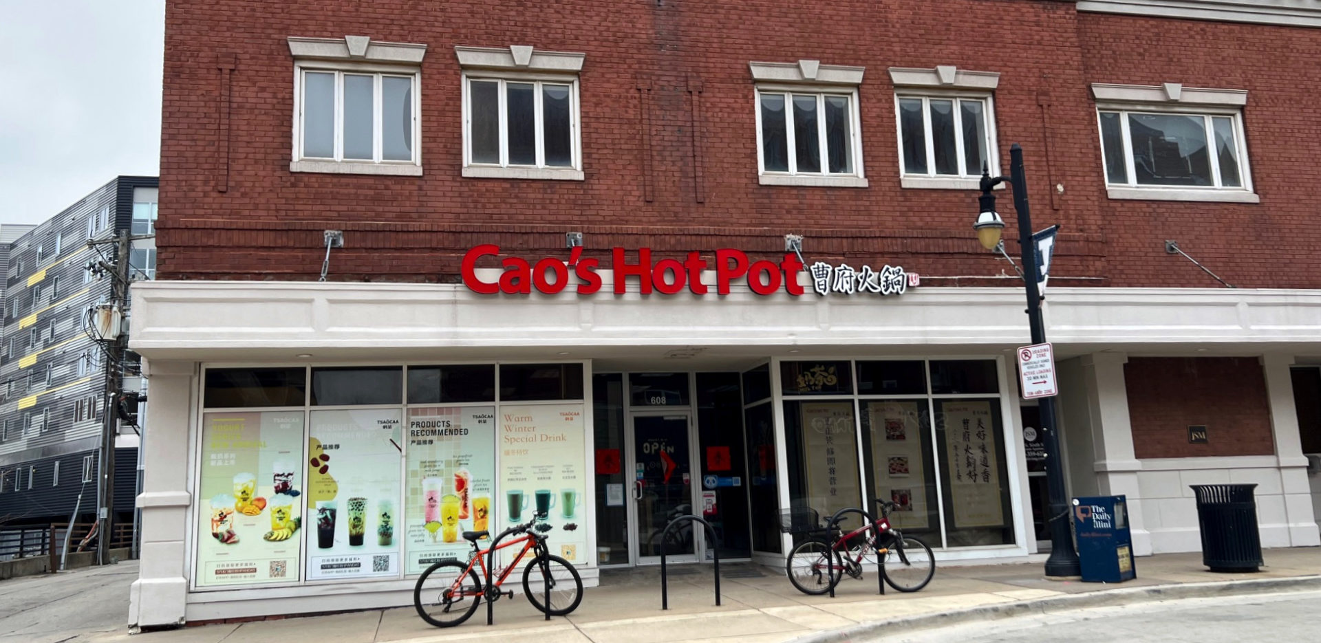 Cao's Hot Pot has a new location on Sixth Street. Red letters with the restaurant's name are affixed to a white covering above the restaurant. Two bikes are parked in front. Photo by Alyssa Buckley.