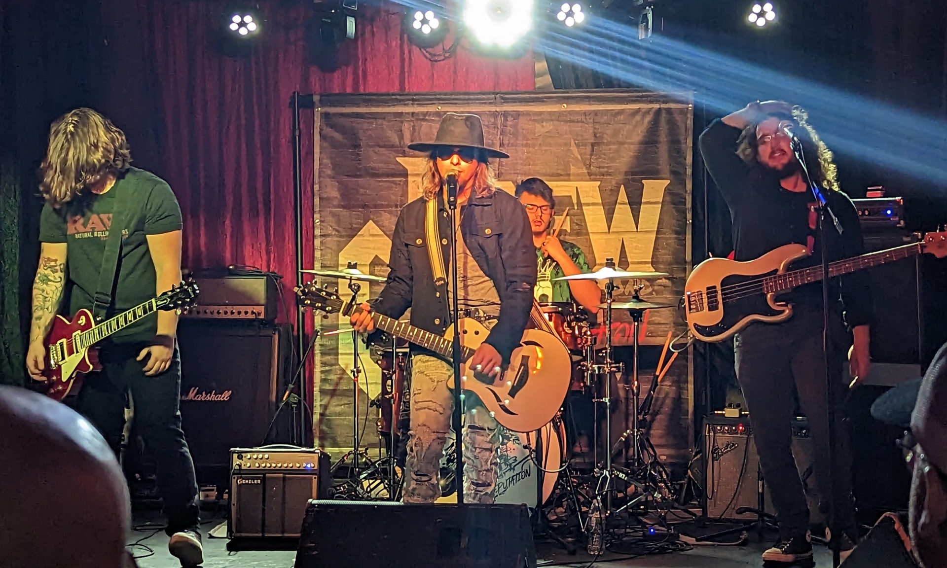 Four band members of Drew Cagle and the Reputation are performing live on a stage.