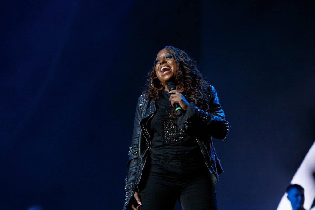 Singer Ledisi holding a mic and singing onstage dressed in all black leather.