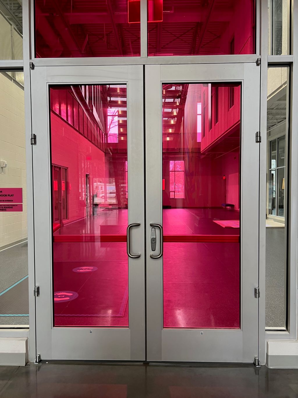 Double glass doors with the glass tinted bright pink, looking into a large open room.