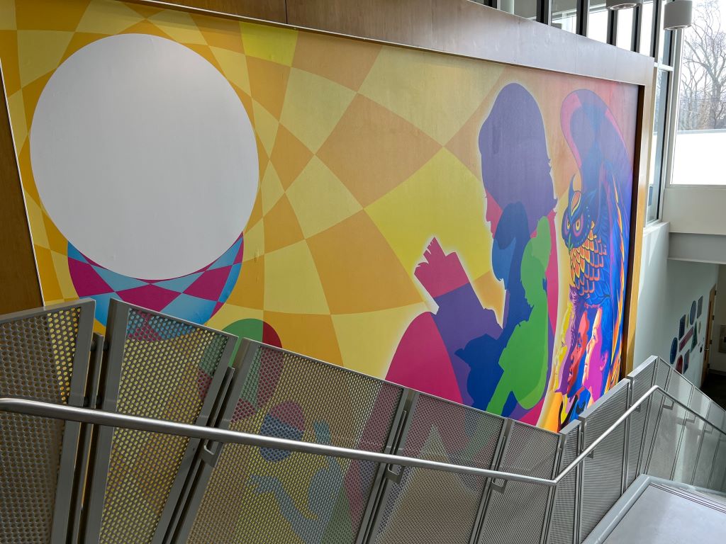 A large wall mural with colorful silhouettes of children against a yellow and gold checked background.