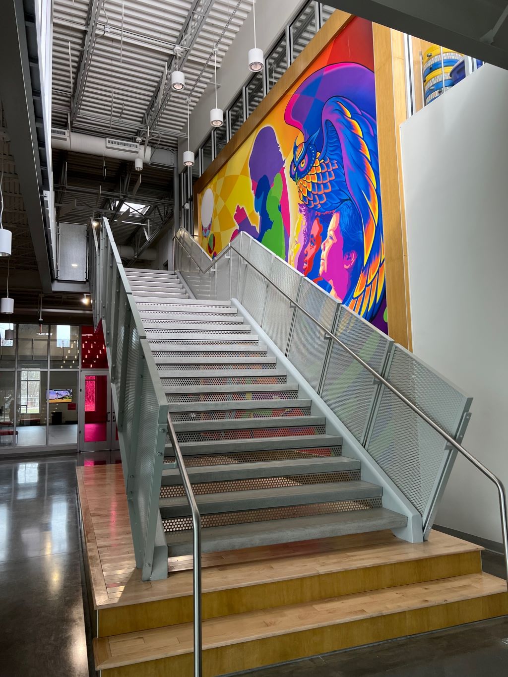 A wide metal staircase on a wooden platform runs along a wall covered in a large colorful mural. 