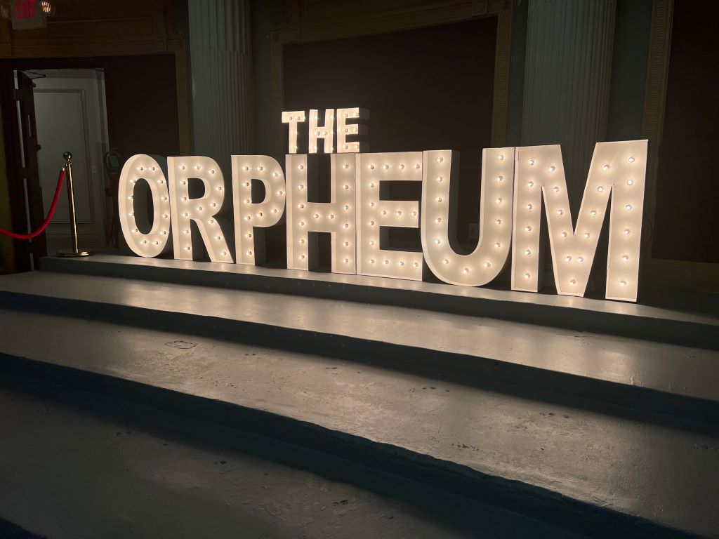 A lighted sign with large block letters that say The Orpheum. It sits on black risers. 