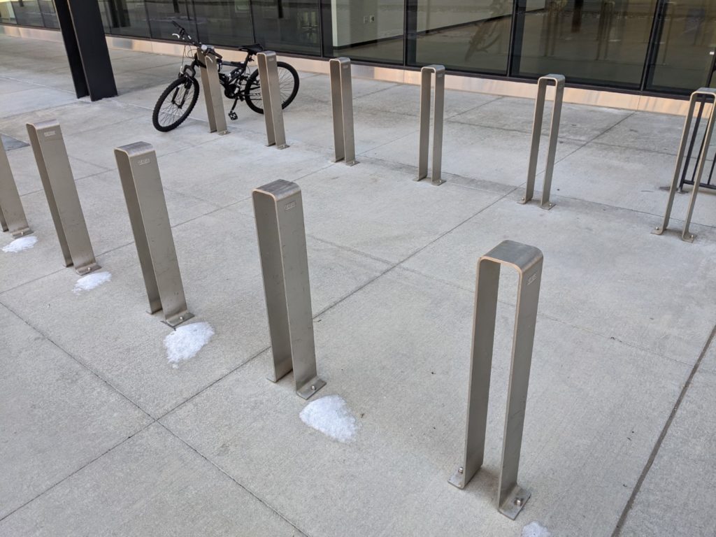 Two rows of metal posts on a sidewalk. There is a bike hooked up to one of them.