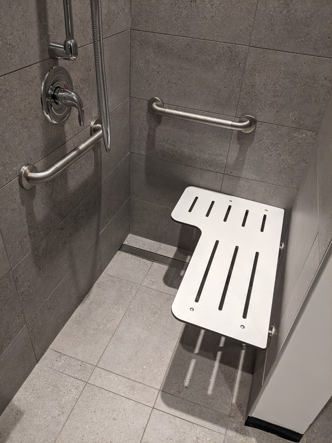 The full shower with shower head attached to the wall, folding bench pushed down.