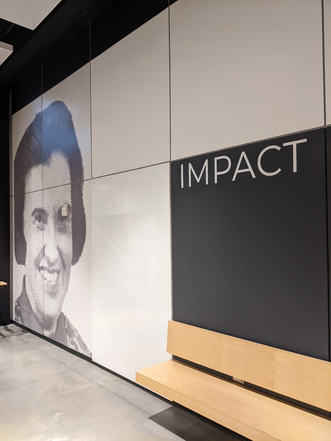 A series of light gray panels on a wall that depict a grayscale pixelated image of a woman on one side. One panel is black with the word IMPACT in white lettering.