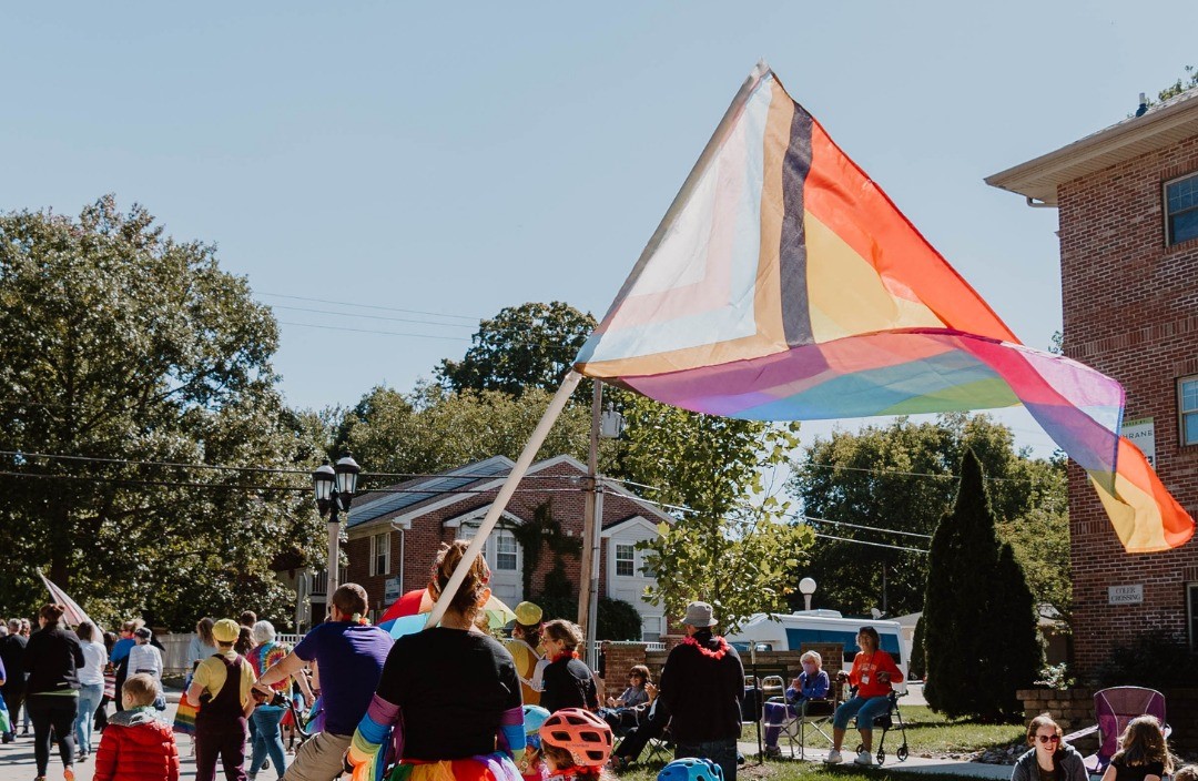 A person in a black shirt is holding a large pride flag as they walk in a parade.