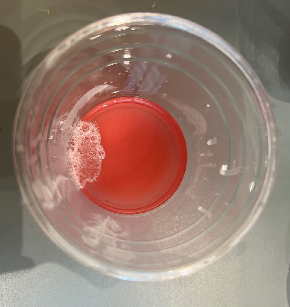 View inside a plastic cup. There is a reddish pink liquid with a cluster of white substance along the edge of the cup.